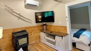 Una camera accogliente con una parete in legno, una TV montata sopra un mobiletto in legno, un letto con una coperta blu e un camino.