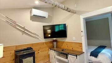 A cozy room with a wooden wall, a TV mounted above a wooden cabinet, a bed with a blue blanket, and a fireplace.