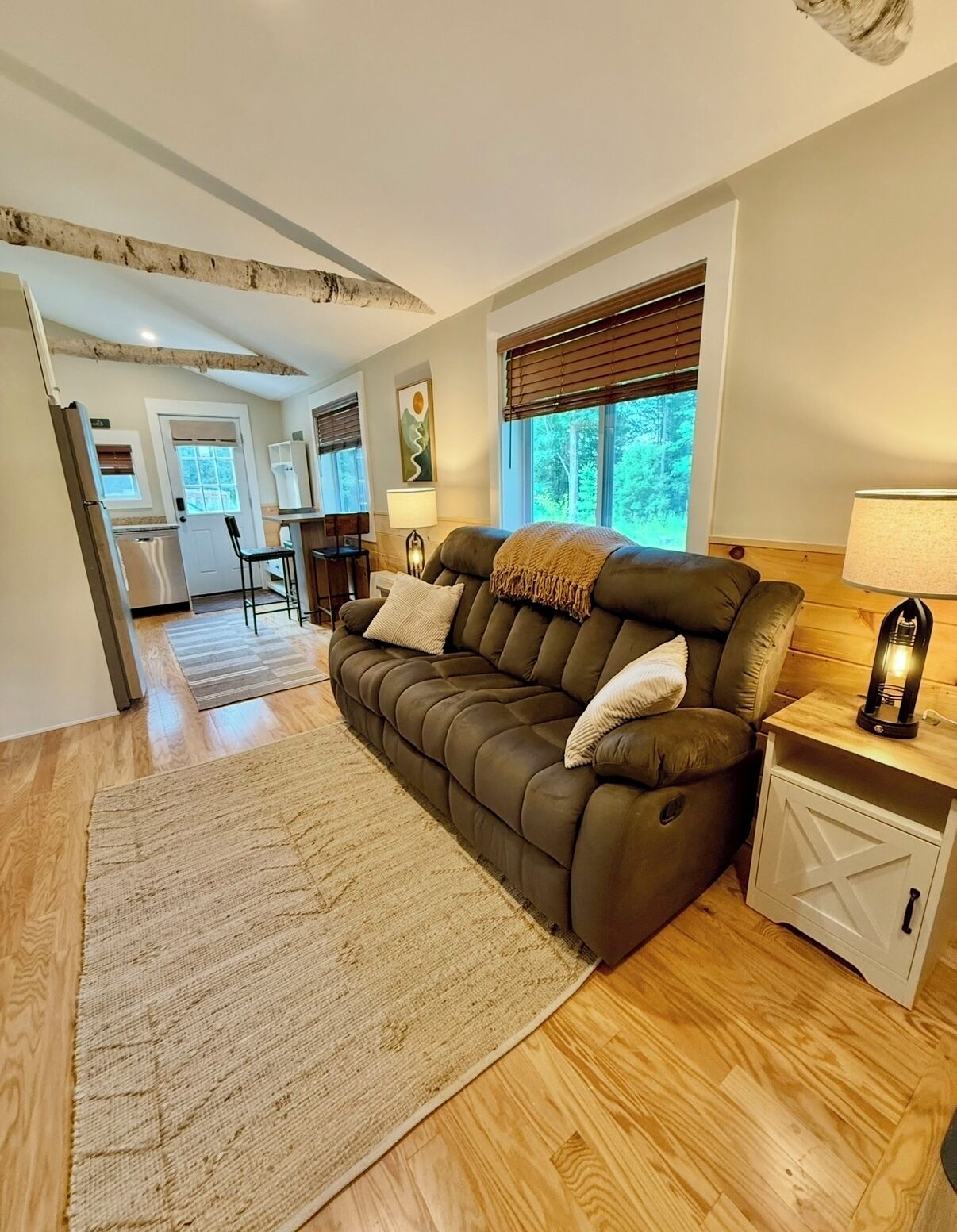 A modern living room with a brown leather sofa, a wooden floor, and a kitchen area in the background.