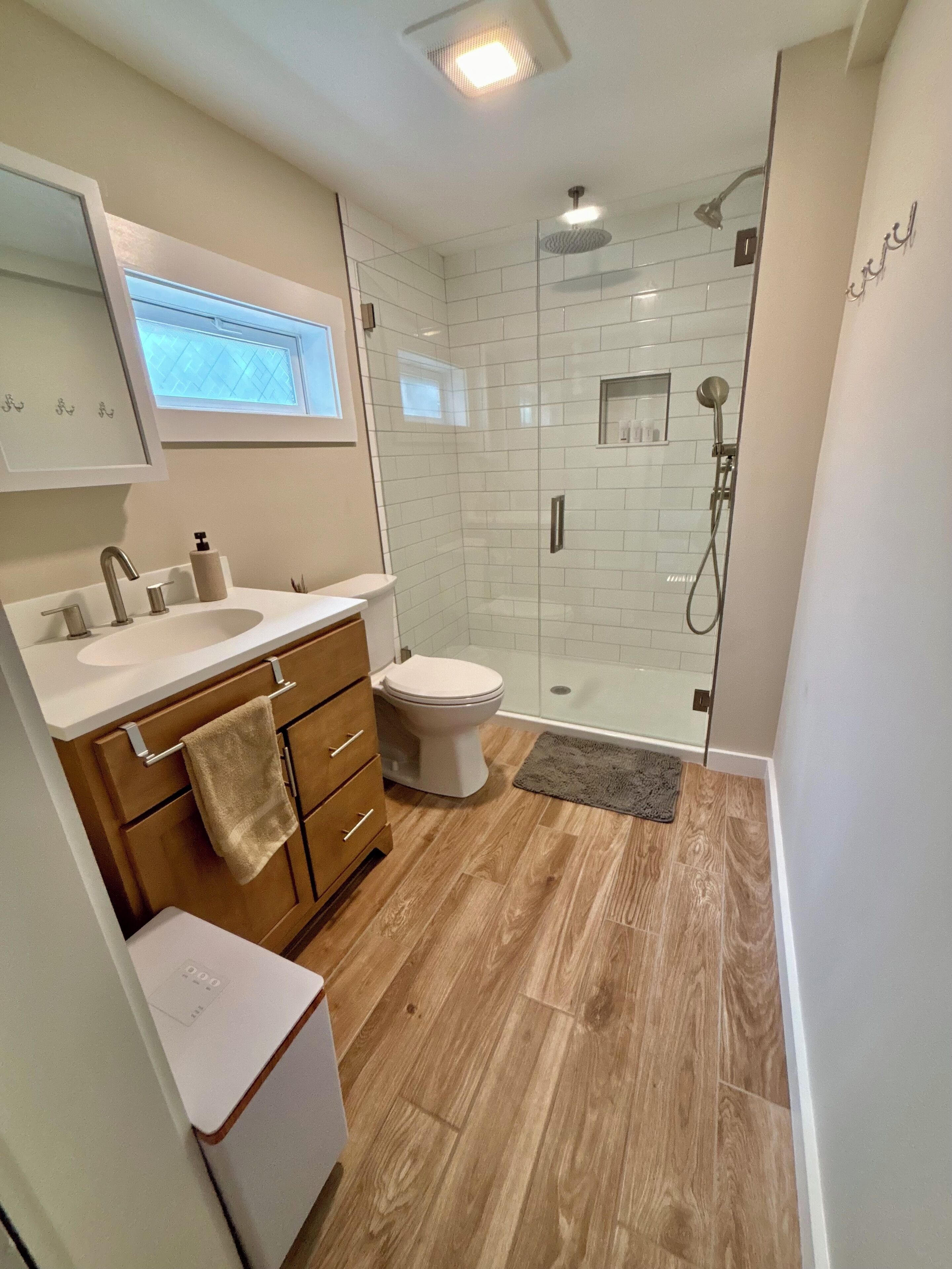 A modern bathroom with a glass-enclosed shower, a toilet, a sink with a mirror, and wooden cabinets.