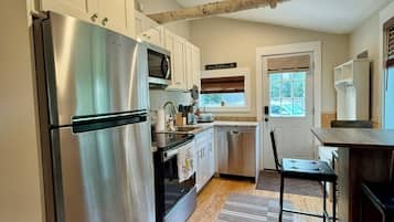 A modern kitchen with a stainless steel refrigerator, wooden cabinets, a built-in oven, and a window with blinds.