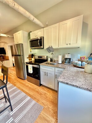 A modern kitchen with stainless steel appliances, white cabinetry, and a granite countertop. - The Birch Retreat — Private Luxury Tiny Home in Bridgton, Maine with AC & WiFi (Bridgton)