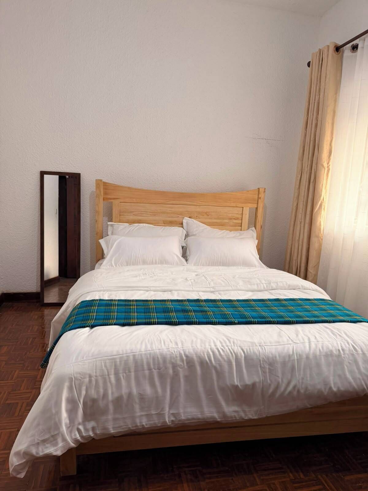 Un lit bien fait, avec une literie blanche et une couverture à carreaux, une tête de lit en bois et un miroir au mur.