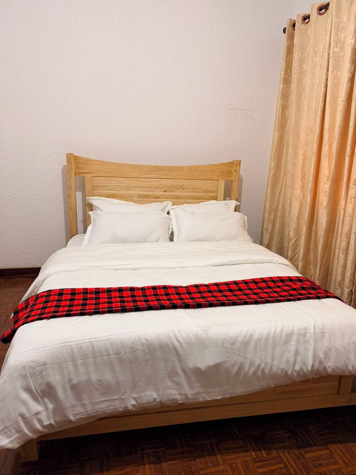 Een eenpersoonsbed met een houten hoofdeinde, wit beddengoed en een rood-zwarte geruite deken.