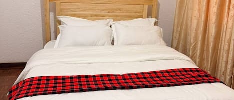 A single bed with a wooden headboard, white bedding, and a red and black checkered blanket.