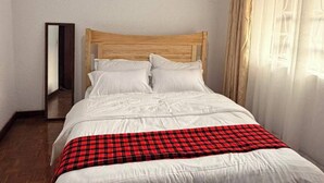 Una camera con un letto singolo, una testiera in legno, biancheria bianca e una coperta a quadretti rossi e neri.