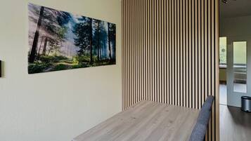 Un comedor con mesa y bancos de madera, un panel de madera vertical y un cuadro con motivos forestales.