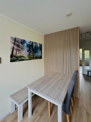 Un comedor con mesa y bancos de madera, un panel de madera vertical y un cuadro con motivos forestales.