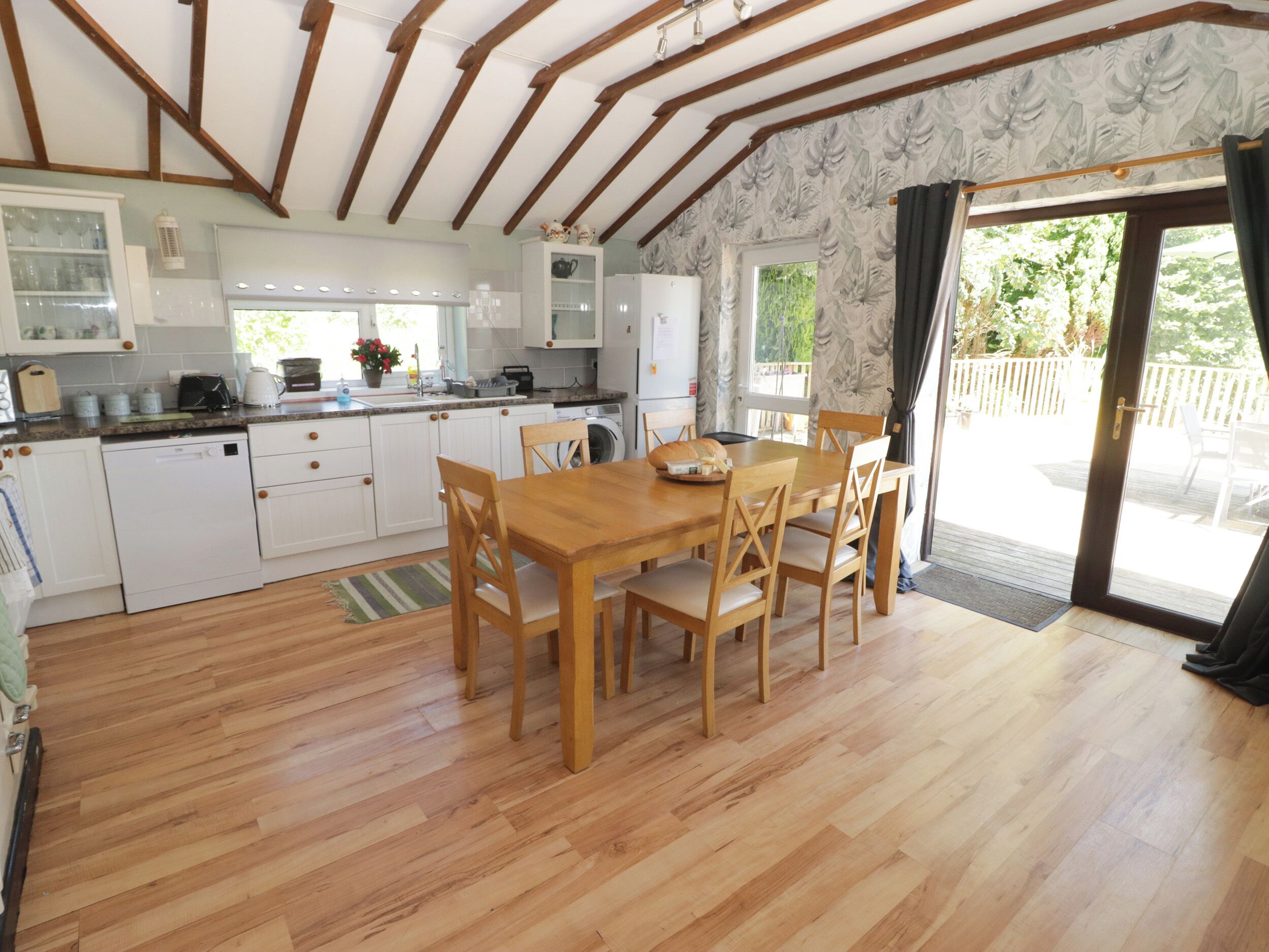 A kitchen with wooden cabinets, a dining table with chairs, and a view of the outdoors through a sliding glass door.