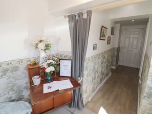 Ein Empfangsbereich mit einem Blumenstrauß, einem gerahmten Willkommensschild und einer Tür mit der Aufschrift 'BATHROOM' im Hintergrund.