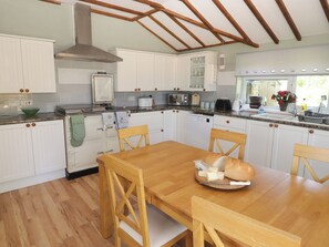 A kitchen with wooden cabinets, a wooden dining table, and a bread basket. - Farm Cottage (Carmarthen)