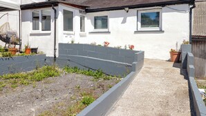 A residential property with a garden bed, potted plants, and a pathway leading to the house. - Farm Cottage (Carmarthen)