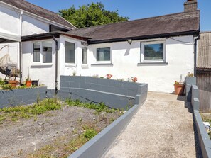 A residential property with a garden bed, potted plants, and a pathway leading to the house. - Farm Cottage (Carmarthen)