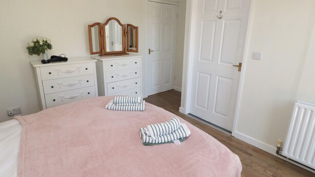 A bedroom with a bed, two bedside tables, a dresser, a mirror, and a door. - Farm Cottage (Carmarthen)