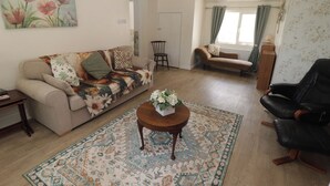 A living room with a sofa, a coffee table with flowers, a patterned rug, and a black leather chair. - Farm Cottage (Carmarthen)