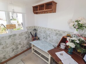 A corner room with a wooden bench, a wooden shelf with hooks, a window with a view, and a desk with papers and a vase of flowers. - Farm Cottage (Carmarthen)