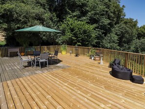 Eine Holzterrasse mit Gartenmöbeln, darunter Stühle und ein Tisch, umgeben von einem Holgitter.