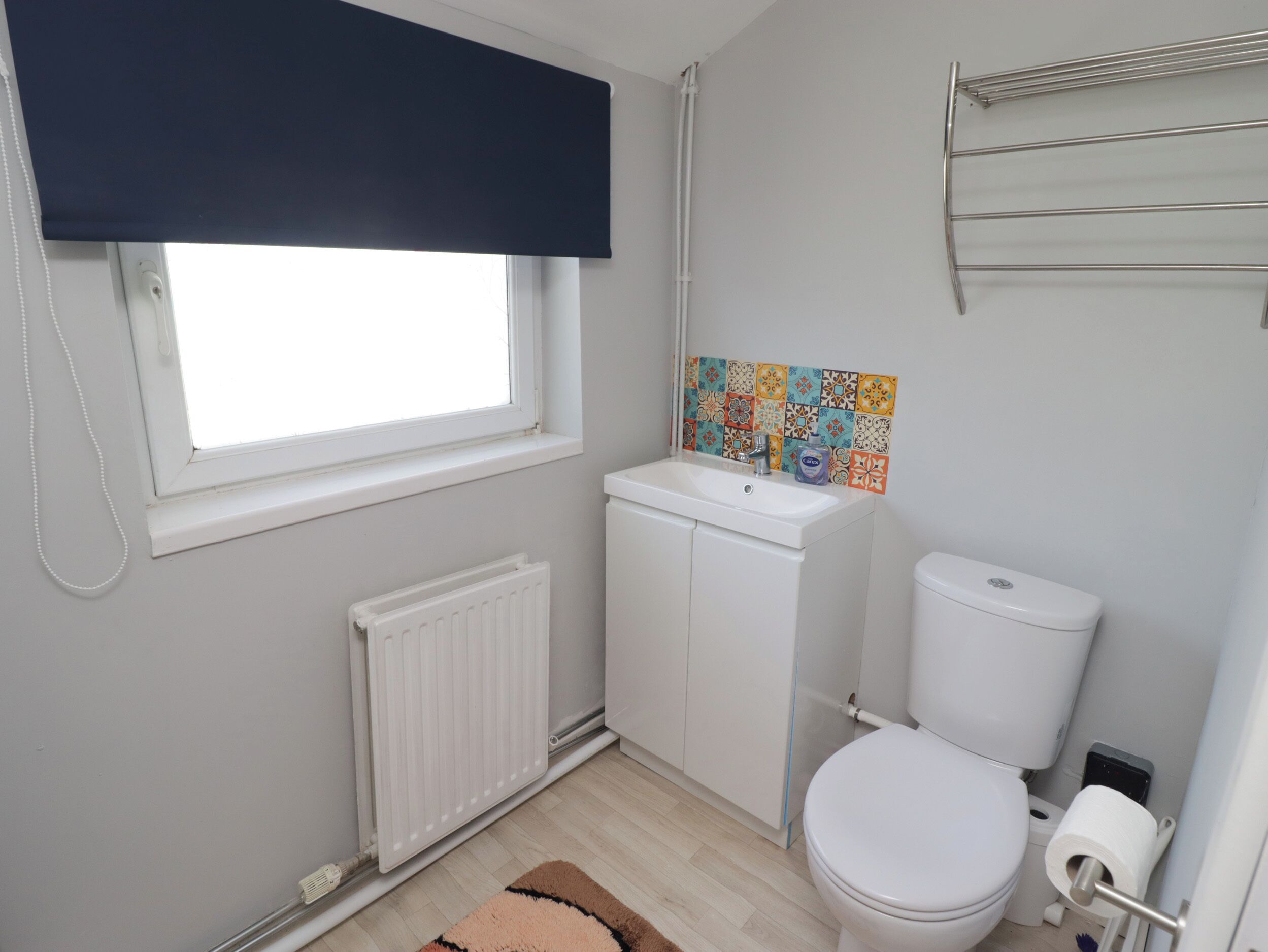 A bathroom with a window, a radiator, a sink, a toilet, and a roll of toilet paper.