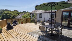 A wooden deck with outdoor furniture, including a table and chairs, and a large umbrella providing shade. - Farm Cottage (Carmarthen)