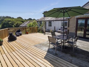 A wooden deck with outdoor furniture, including a table and chairs, and a large umbrella providing shade. - Farm Cottage (Carmarthen)