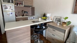 A compact kitchen with a central island, bar stools, a refrigerator, and a coffee maker. - Bright studio apartment 50 meters from the beach (Mauguio)