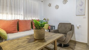 Una sala de estar con un sofá, una mesa de madera con una planta, un sillón gris y decoración en las paredes.