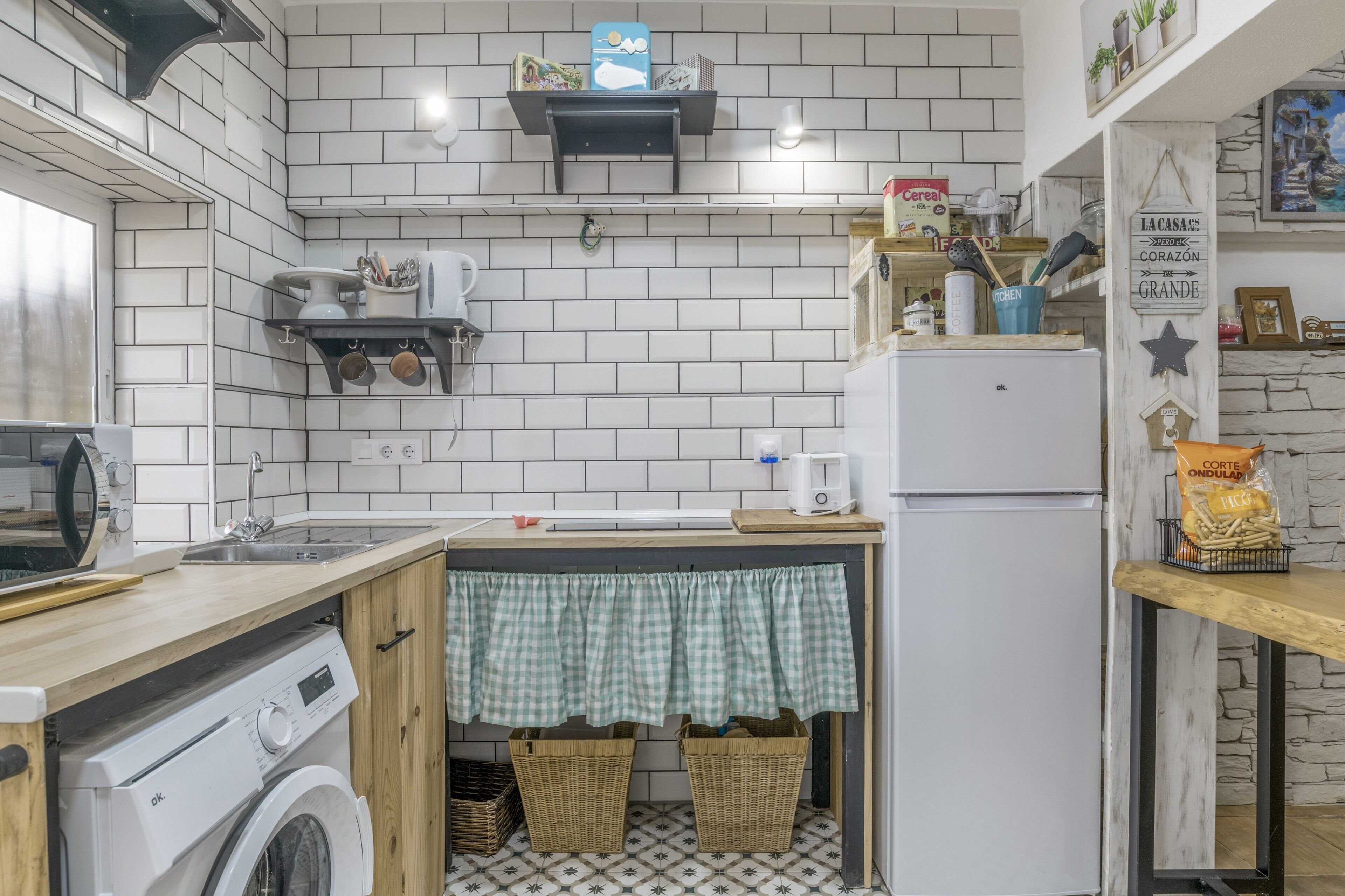 Een compacte keuken met een wasmachine, een spoelbak, een koelkast en een klein plankje met keukenbenodigdheden.