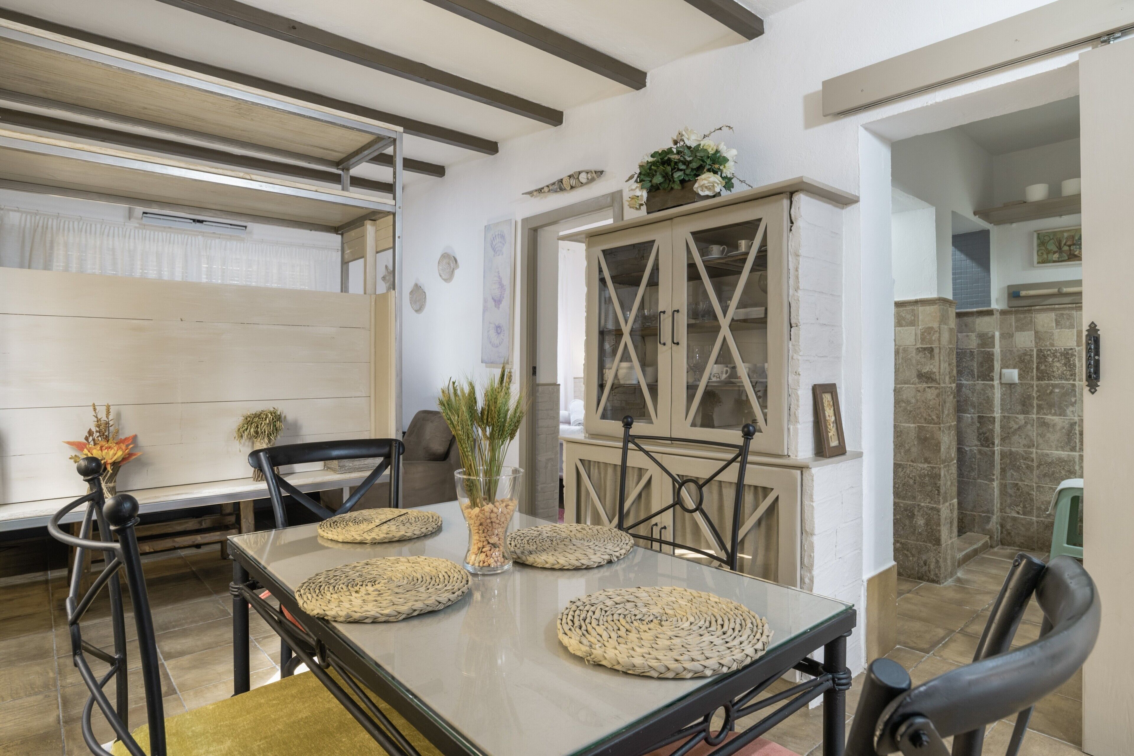Un coin repas avec une table dressée pour quatre personnes, un meuble avec des portes en verre et une cuisine visible au fond.