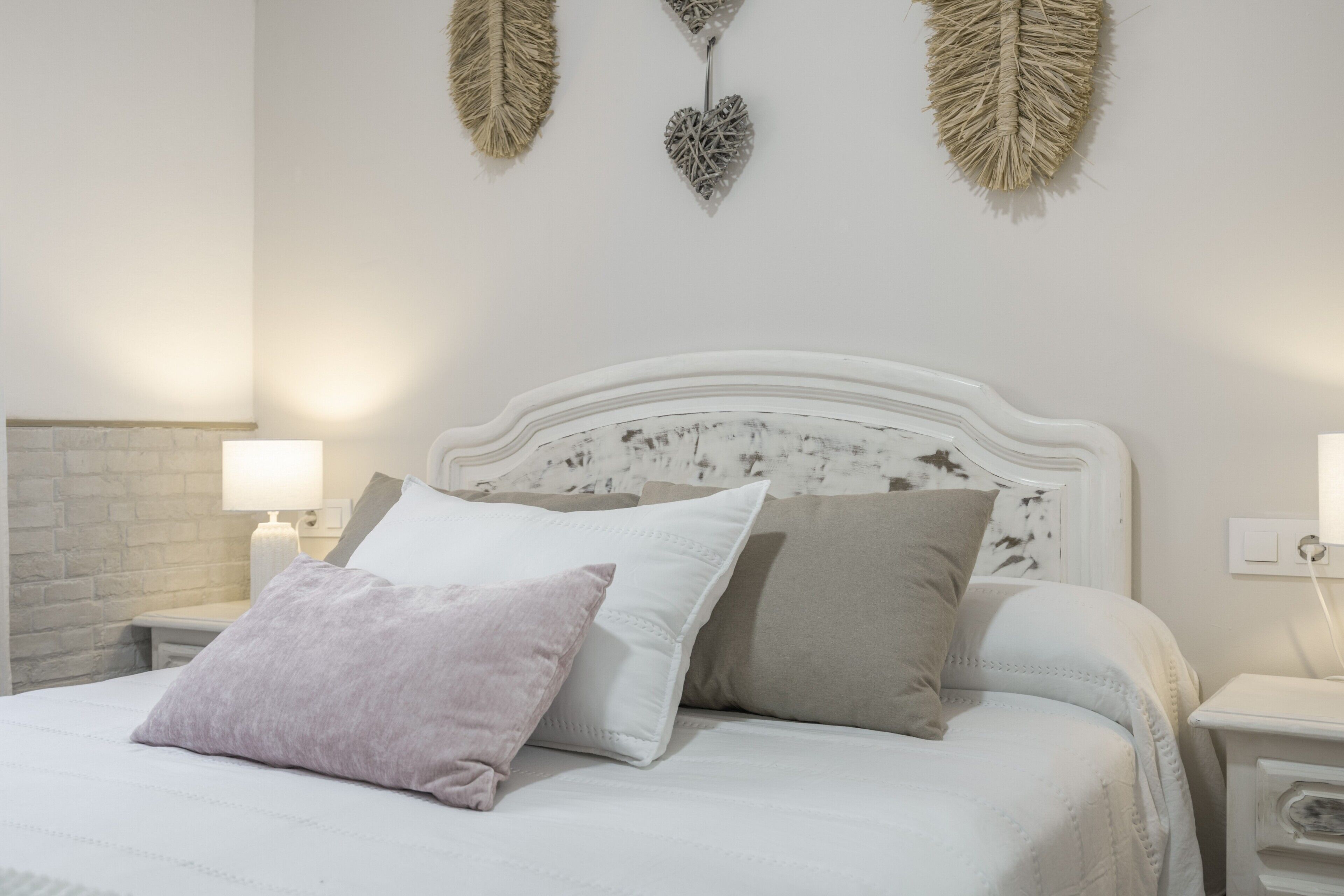 A bed with white bedding and multiple pillows, a white headboard, and wall-mounted decorative items.