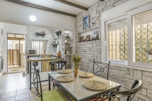 A modern kitchen with white brick walls, a dining area with a glass table, and a view through a window with a metal grid. - Seafront Apartment in El Palmar, Cádiz (El Palmar de Vejer)