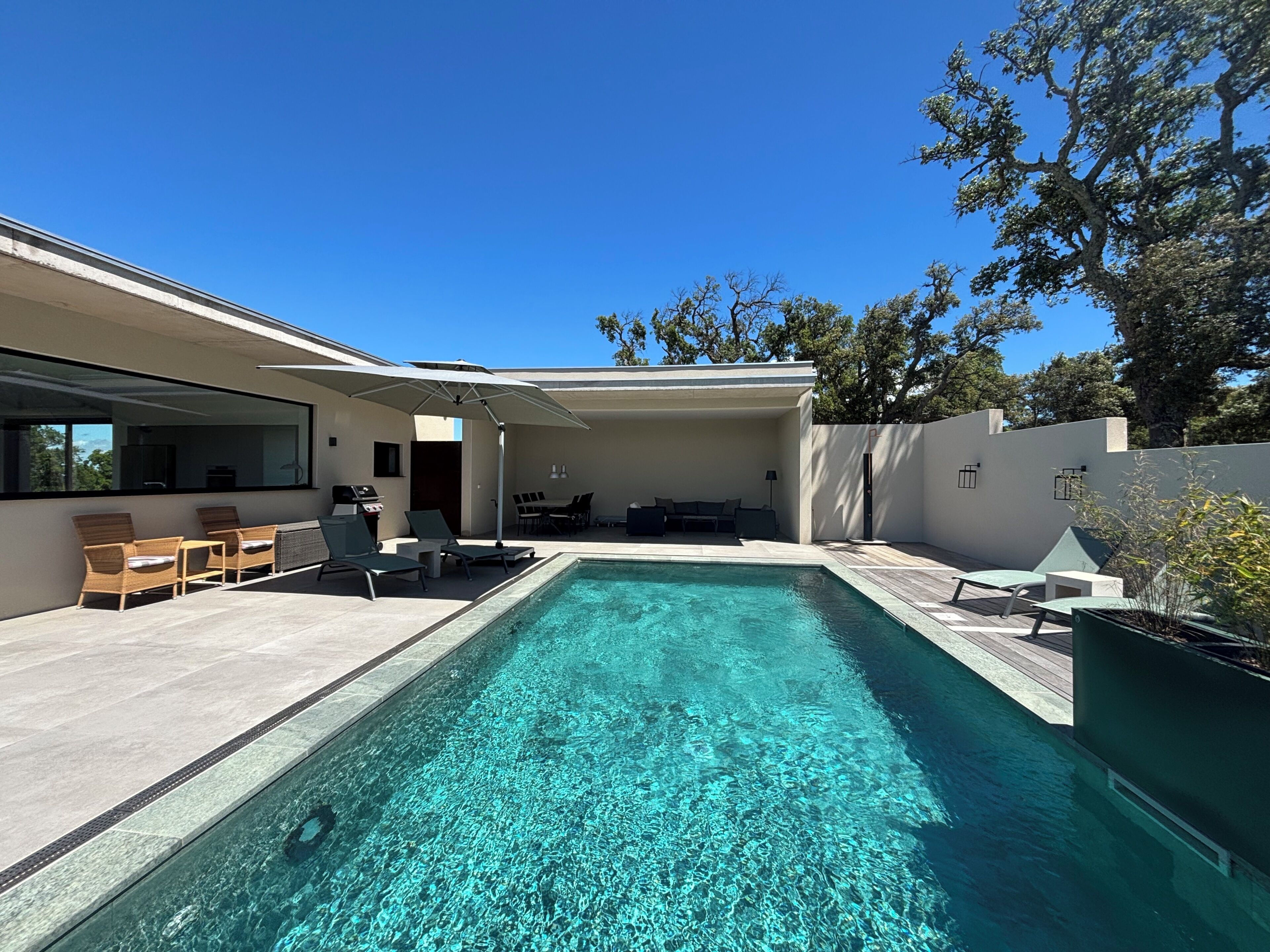 A modern outdoor pool area with lounge chairs, a barbecue, and a covered seating area.