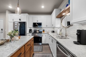 A modern kitchen with white cabinetry, stainless steel appliances, and a marble countertop. - New Egg Harbor Condo • Steps to Shipwrecked, Marina & Beach • 2 King Suites (Egg Harbor)