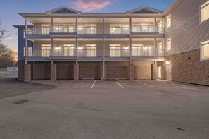 A multi-story building with balconies, a stone facade, and a parking area. - New Egg Harbor Condo • Steps to Shipwrecked, Marina & Beach • 2 King Suites (Egg Harbor)