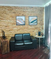 Una habitación con pared de madera, un sofá negro, una pequeña mesa redonda con una bandeja y arte abstracto en la pared.