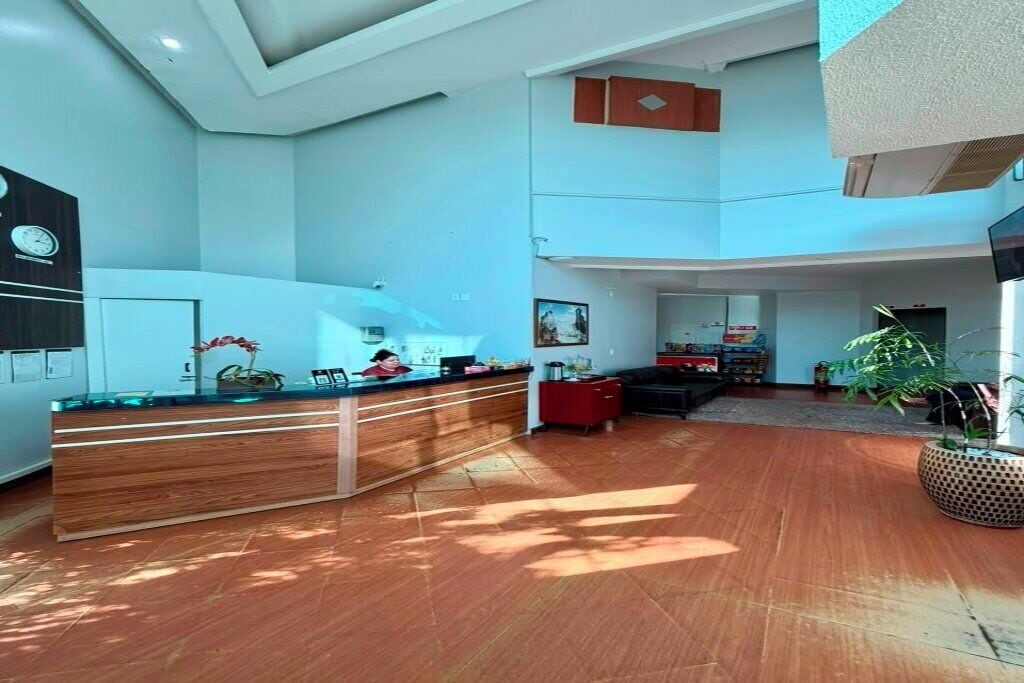 Um lobby espaçoso com uma mesa de recepção, área de estar e uma grande planta.