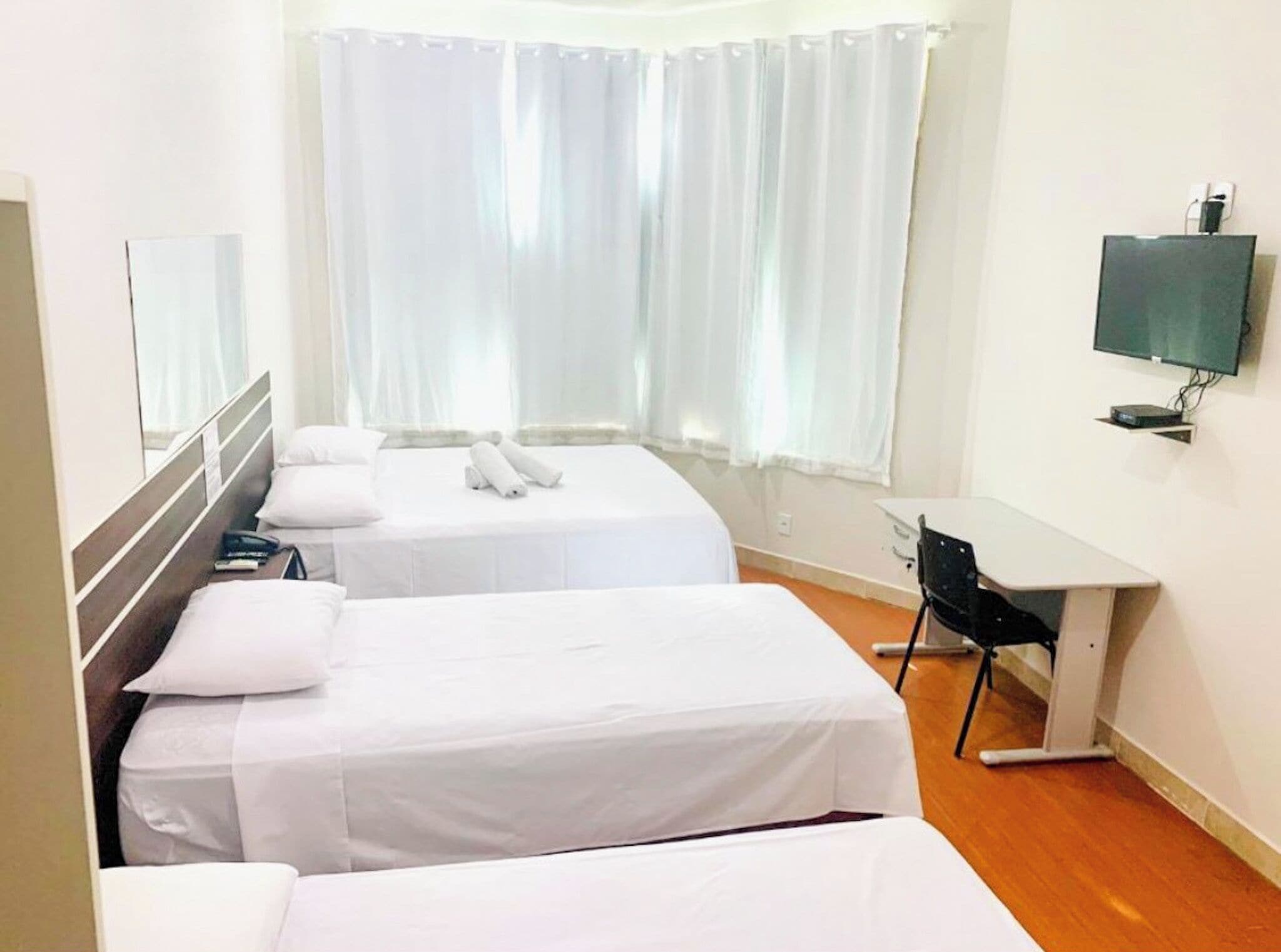 Quarto de hotel com duas camas, uma escrivaninha, televisão e uma janela com cortinas.