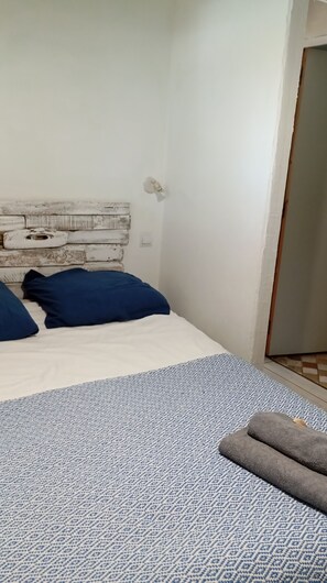 Ein Schlafzimmer mit einem Bett, Kissen, einer Wandleuchte und einem gemusterten Teppich.