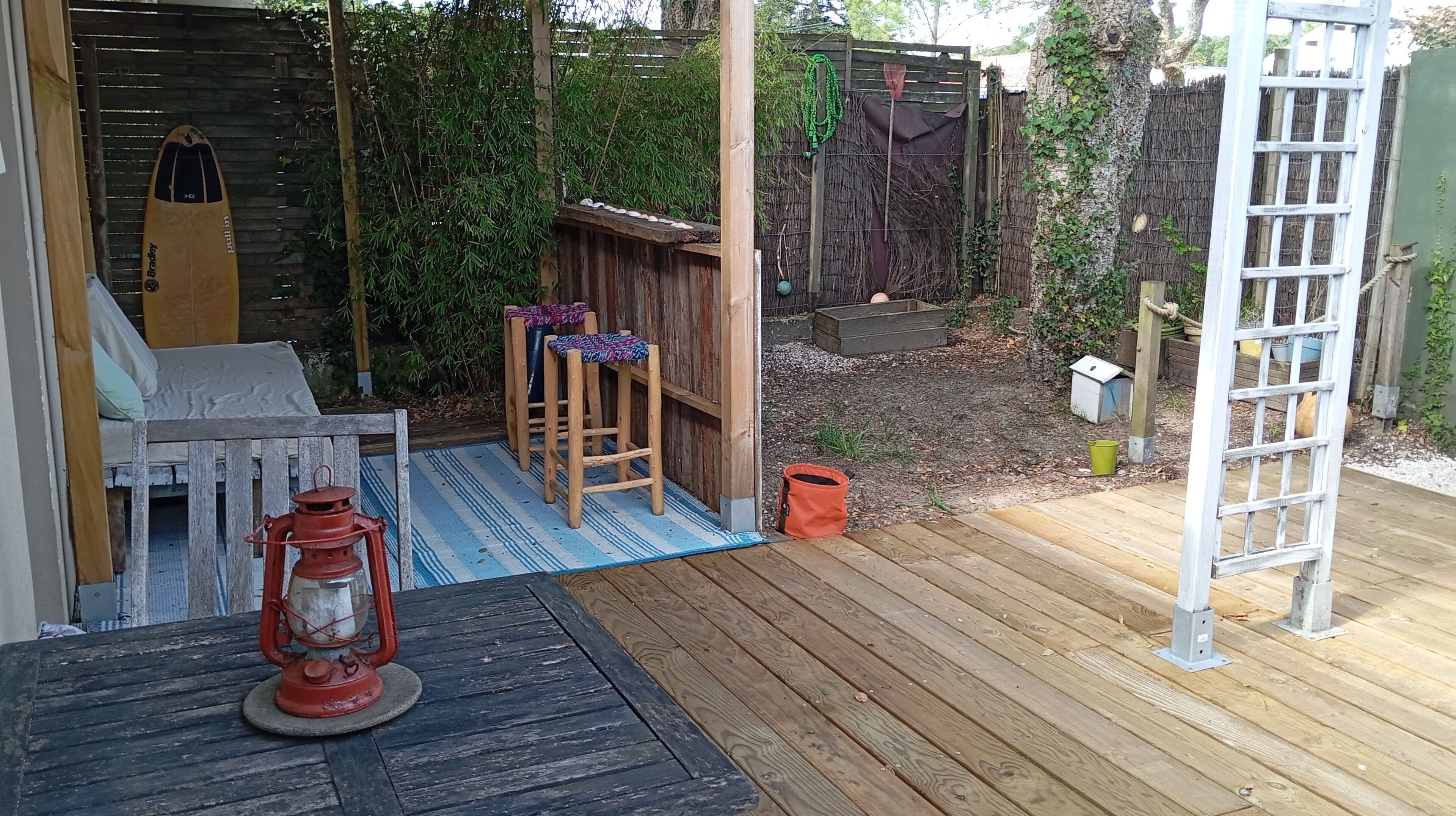 Une terrasse en bois avec un banc et une table, une échelle et un petit espace jardin agrémenté d’une clôture.