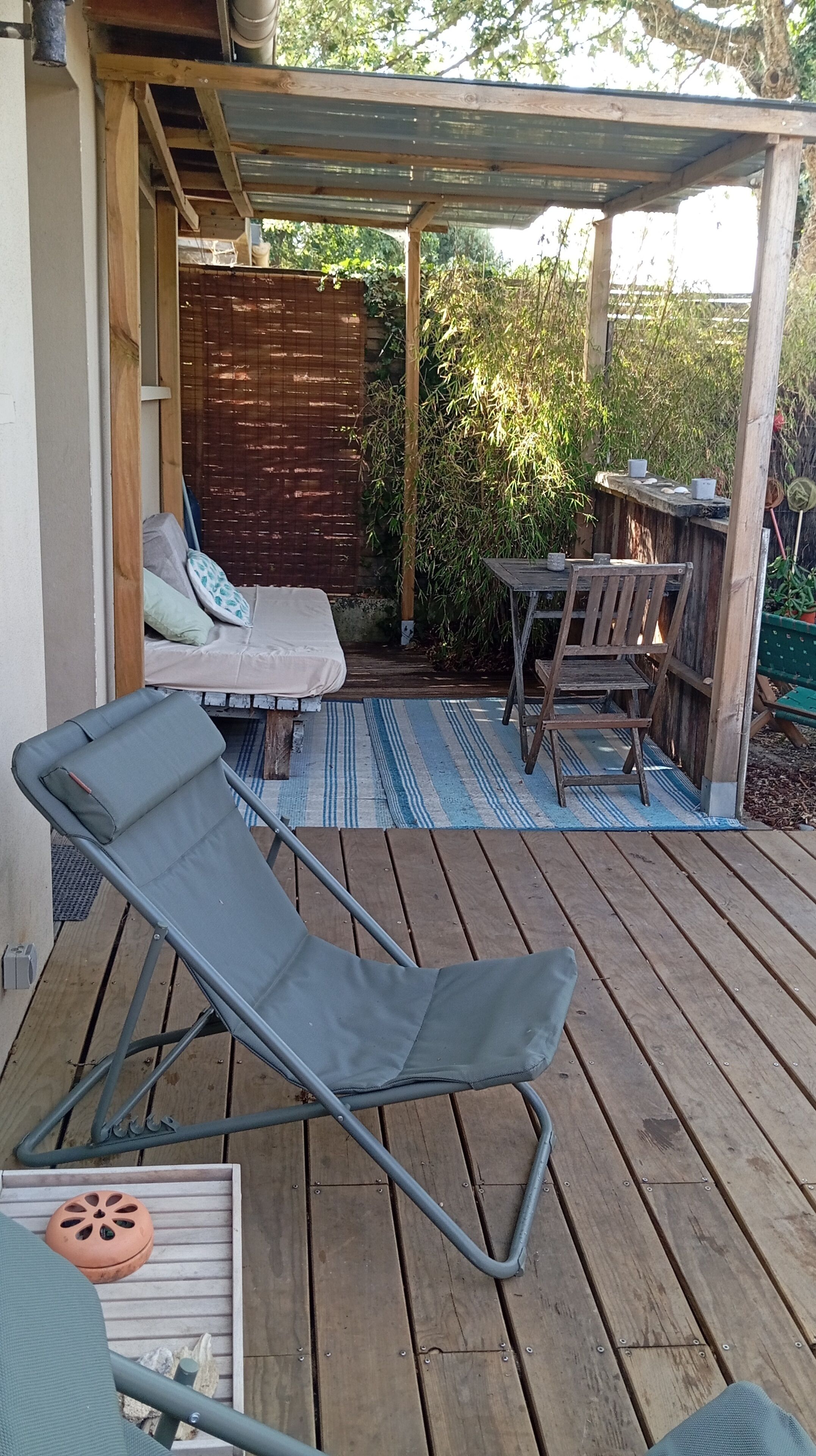 Une terrasse en bois avec un fauteuil de relaxation, une petite table et un espace salon abrité.