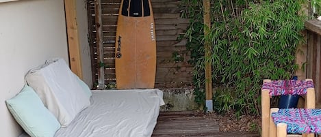 Une terrasse en bois avec un lit, une planche de surf et une chaise.