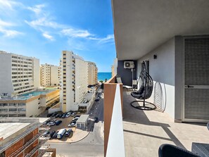 Un balcón con vista al mar, una silla colgante y una zona de piscina.