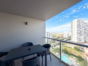 Un balcón con mesa y sillas, con vistas a un paisaje urbano y una piscina.