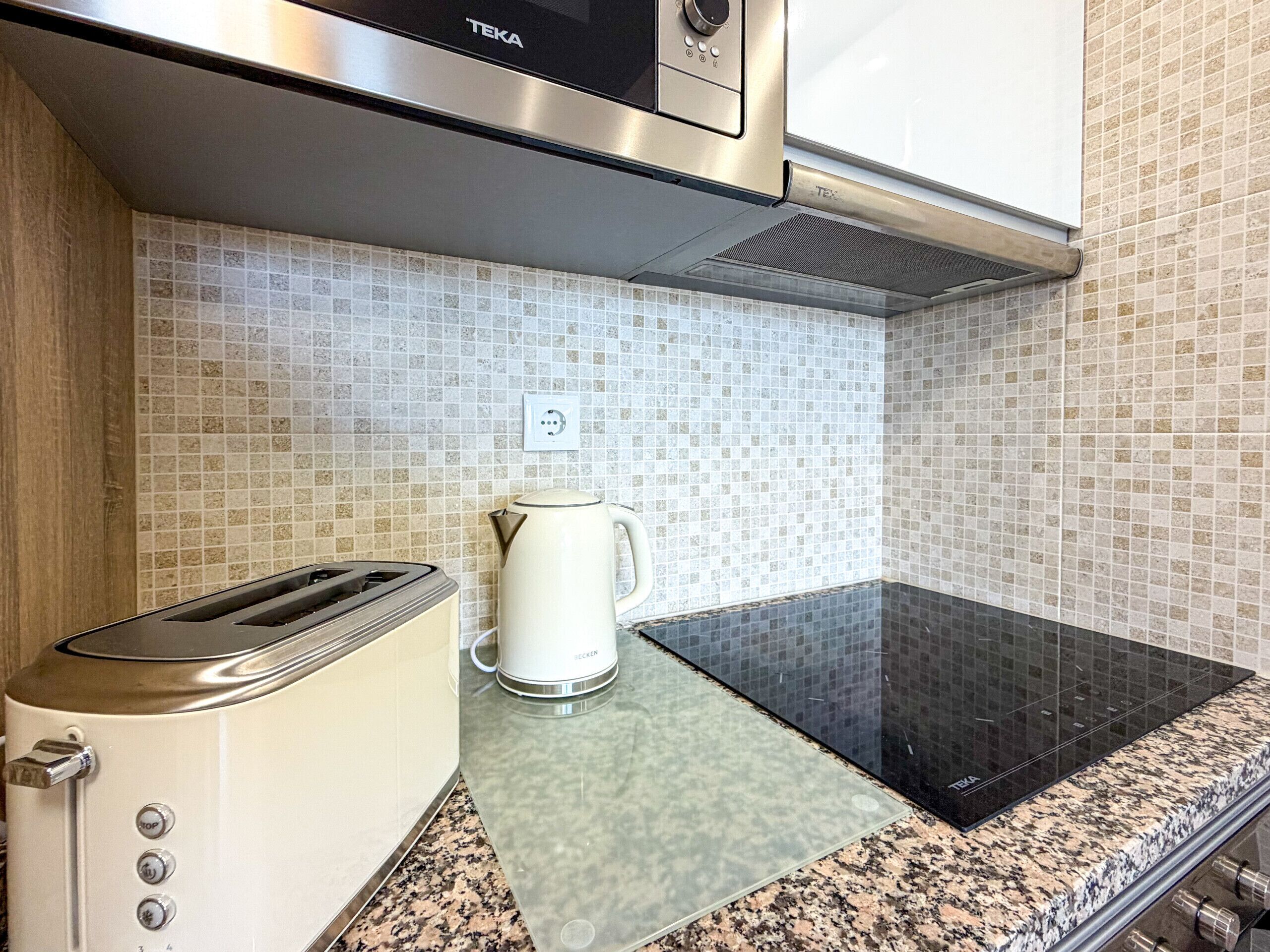 A kitchen with a toaster, a kettle, and a black induction cooktop.