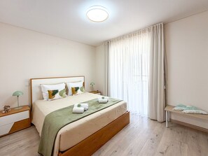 A hotel room with a bed, a nightstand, a lamp, a bench, and a window with curtains. - Apartment Praia Rocha | Elite Residence | Prestige (Portimão)