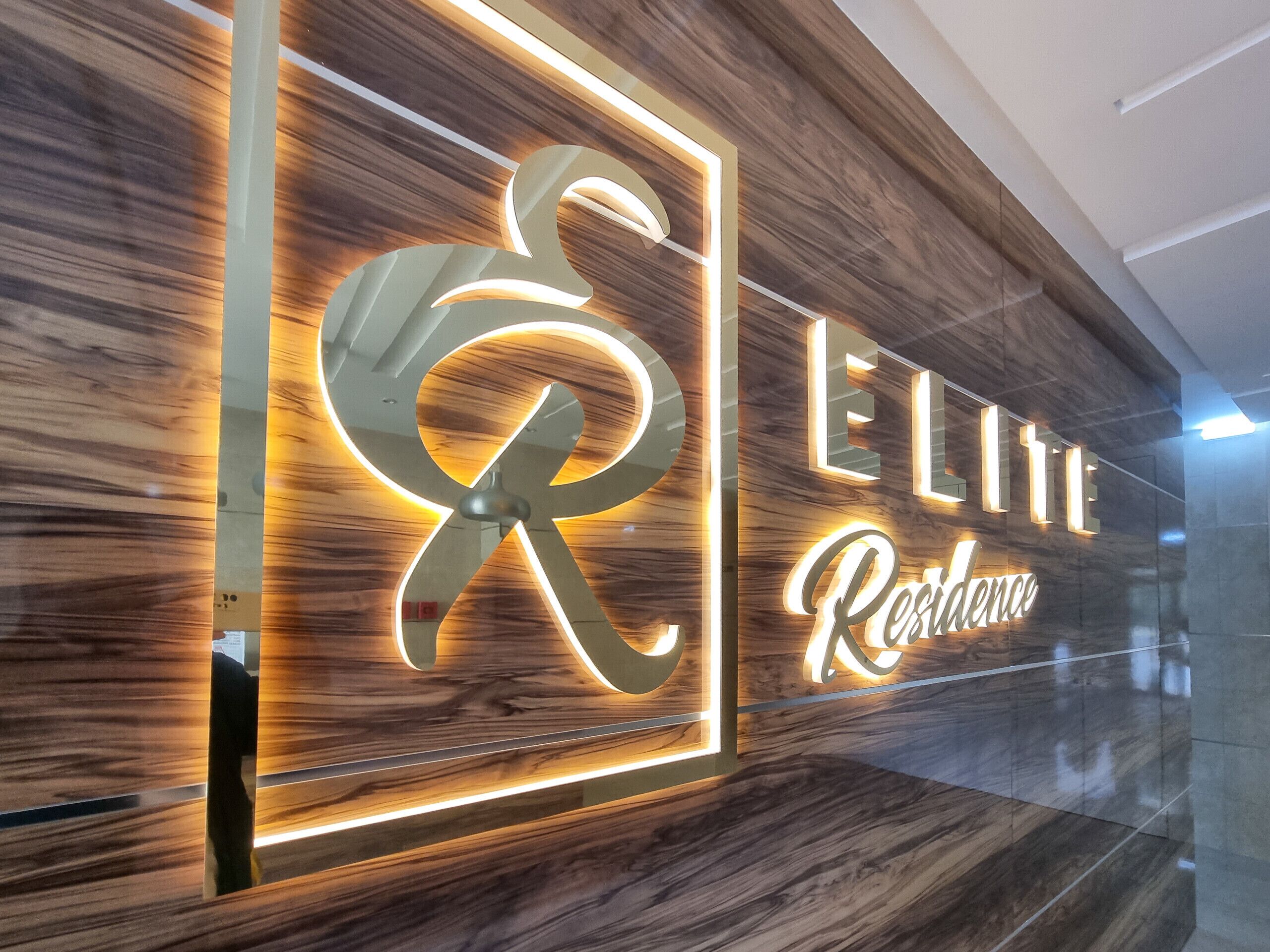 A hotel sign with illuminated letters spelling 'ELITE Residence' on a wooden wall.
