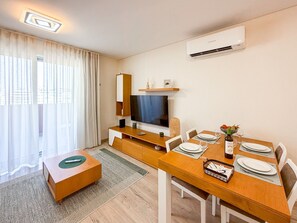 Ein modernes Hotelzimmer mit Essbereich, einem Flachbildfernseher, einer Klimaanlage und Blick aus dem Fenster.