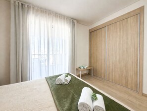A hotel room with a bed, a green textured rug, a wooden wardrobe, and a small table with towels. - Apartment Praia Rocha | Sea View | Prestige (Portimão)