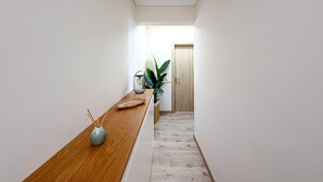 Een smalle gang met een houten bankje, een vaas met rietverspreiders, en een potplant.