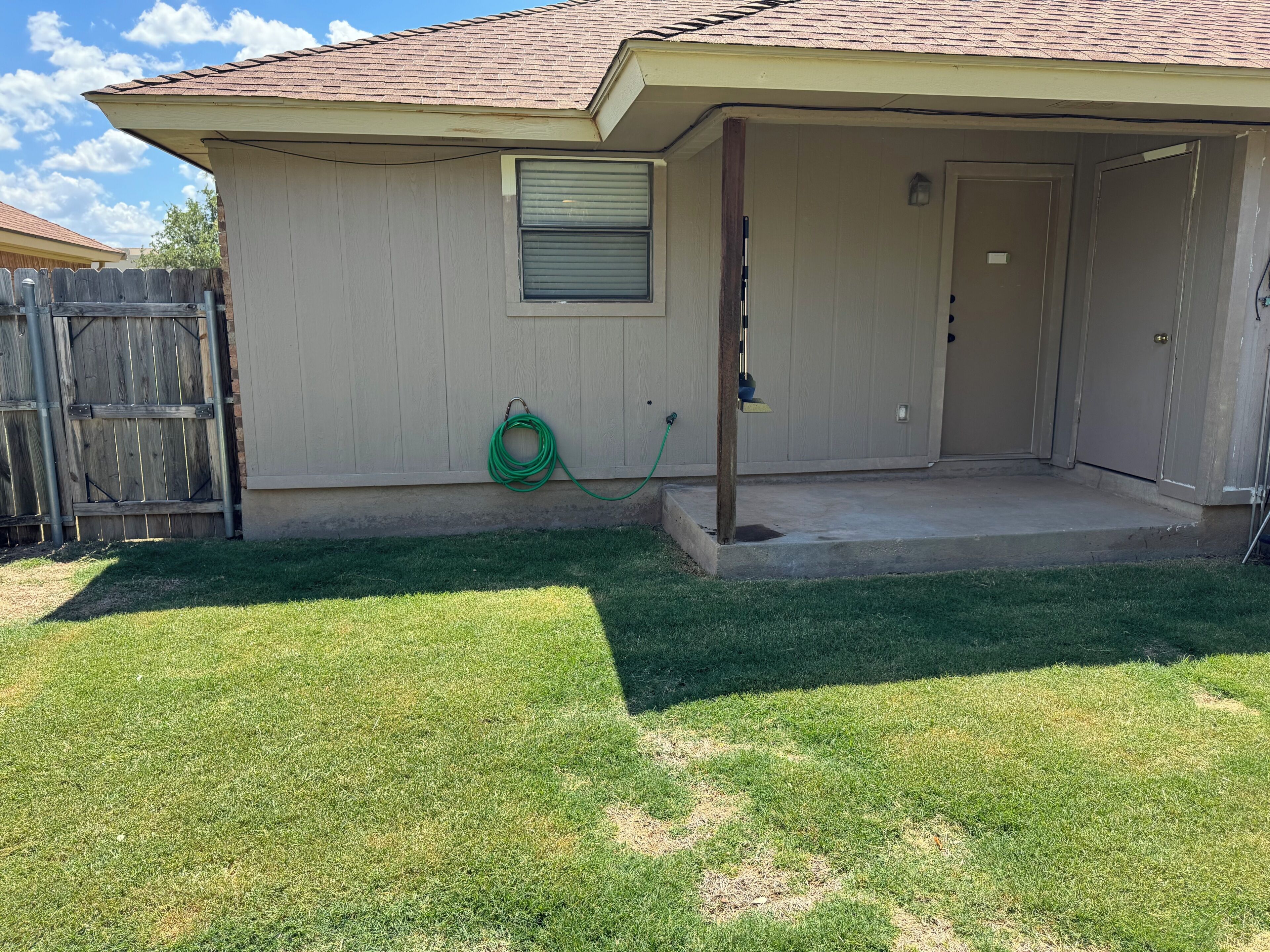 A residential house with a covered porch, a wooden fence, and a green garden hose.
