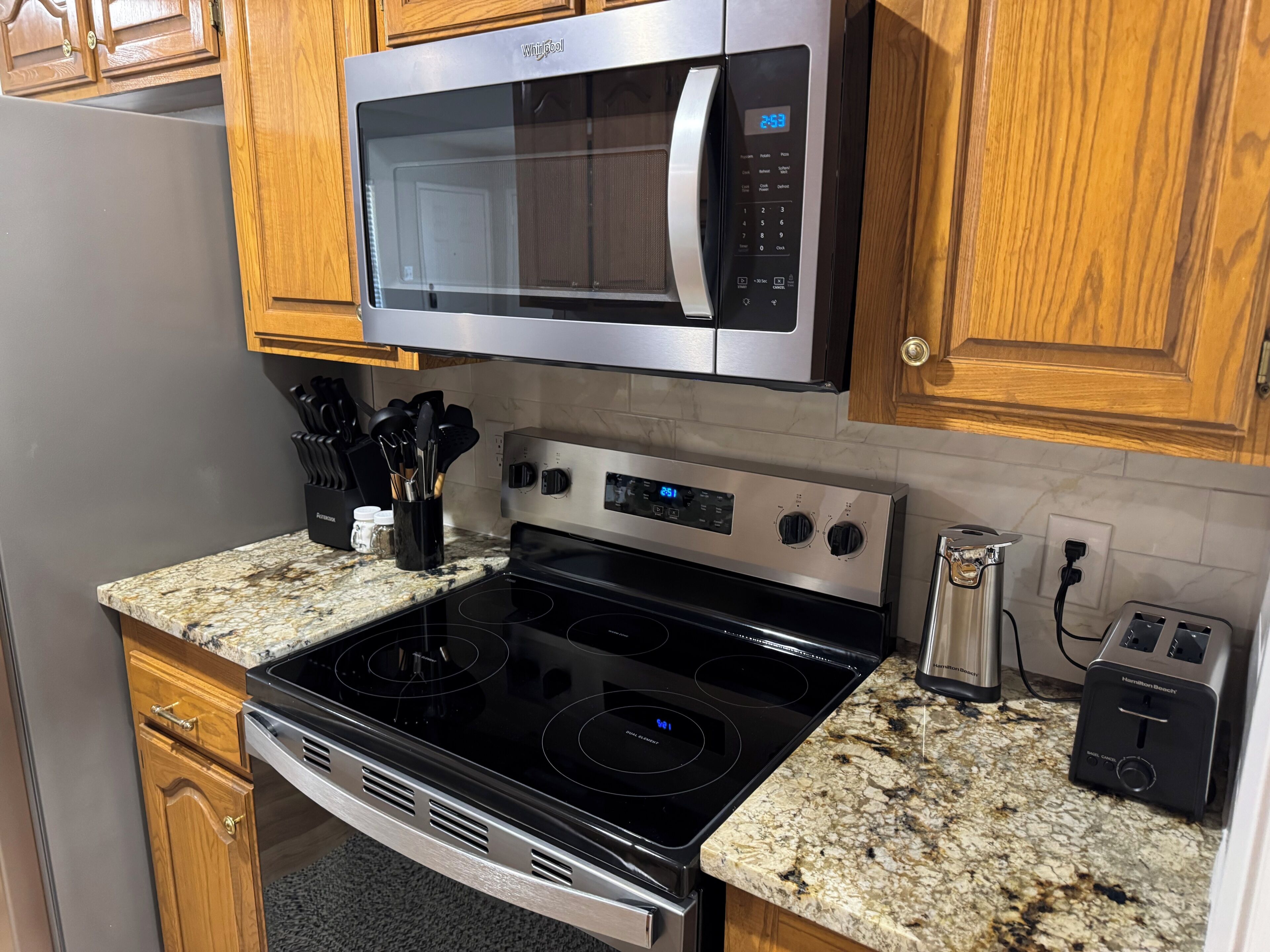 A kitchen with a stainless steel microwave, a black stove, and a granite countertop.